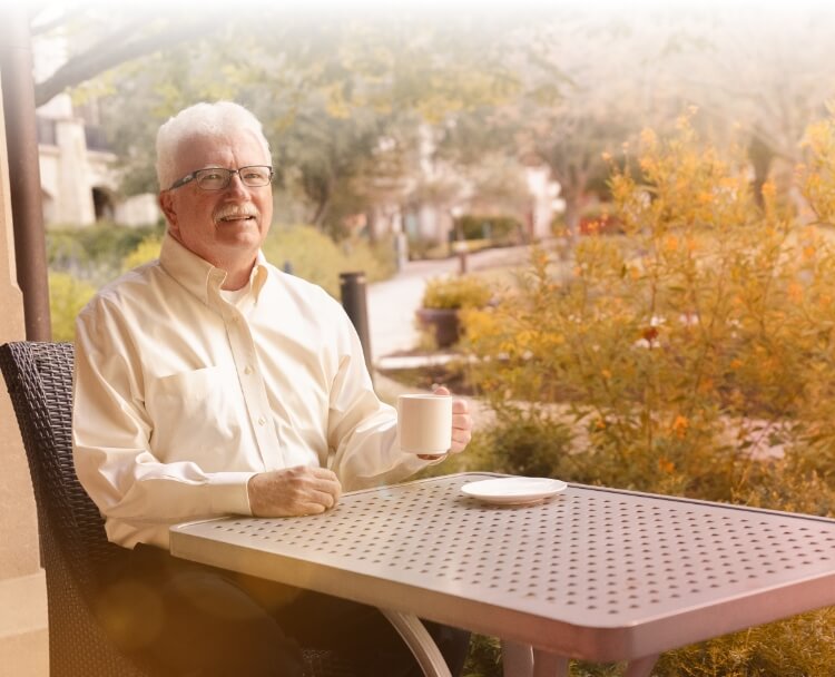 Gary, treated with AMVUTTRA® (vutrisiran), sitting at a table in a park on a sunny day.